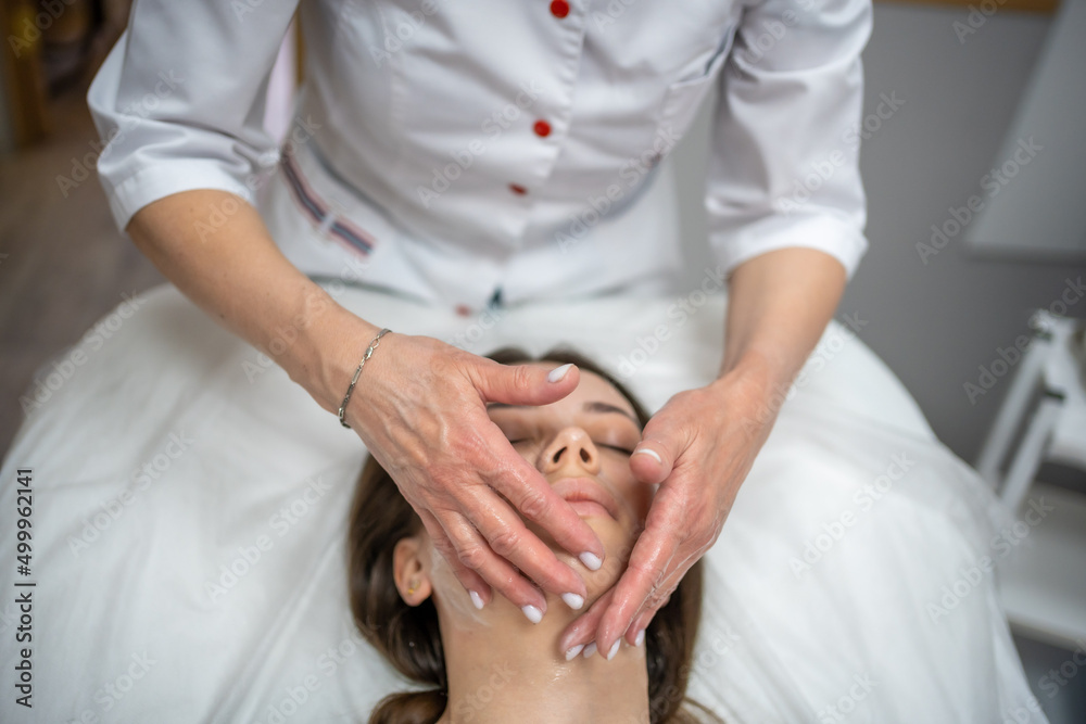 Face massage. Portrait of woman on cleaning face procedure by woman cosmetologist in beauty clinic. Beauty industry concept. Face massage. Portrait of woman on cleaning face procedure by woman cosmetologist in beauty clinic. Beauty industry concept.