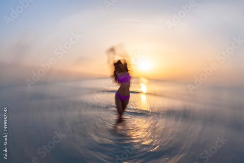 Motion blurred Asian female dancing in ocean sunrise