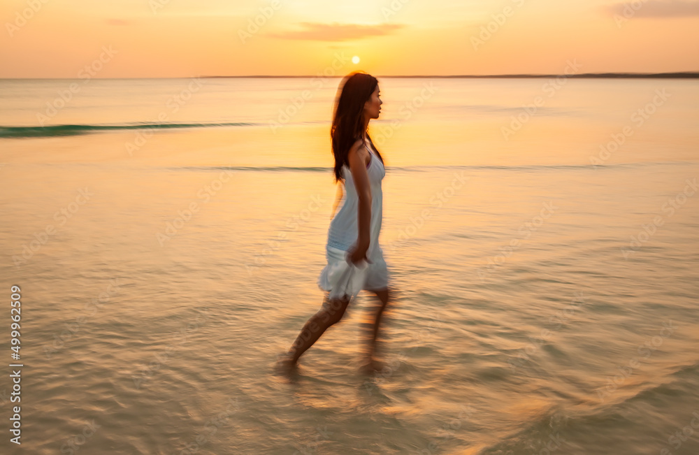 Asian woman walking through ocean with motion blur