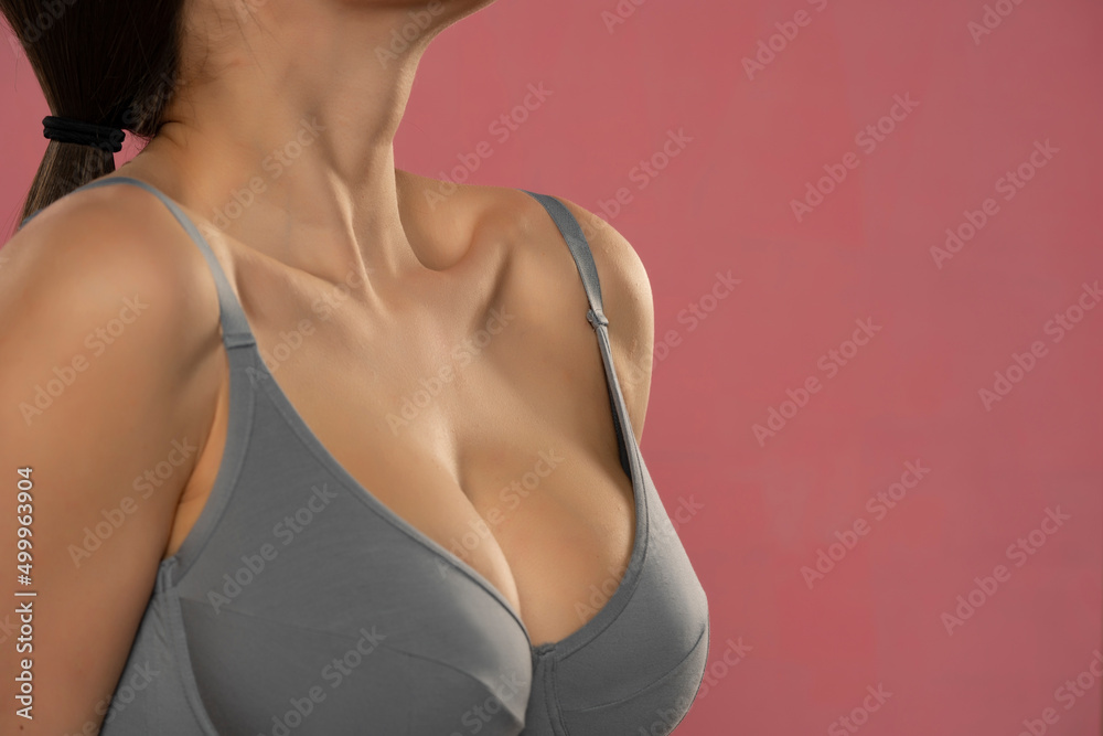Large and beautiful women breasts in gray bra on pink background - obrazy, fototapety, plakaty 