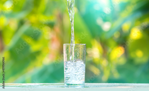 Drink water pouring in to glass over sunlight and natural green background.Water splash  in glass.water pouring into glass on green blurred background.