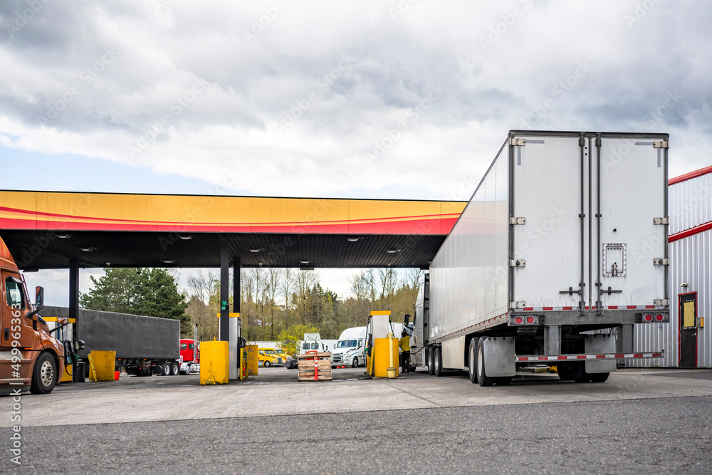 Truck driver refills the big rig semi truck tanks at the truck stop gas station to continue the cargo delivery Truck driver refills the big rig semi truck tanks at the truck stop gas station to continue the cargo delivery