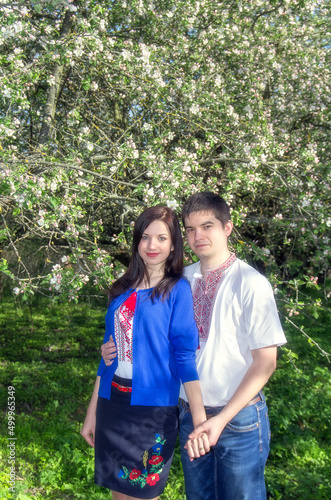A young loving couple man and woman in embroidered shirts near a flowering tree in a spring garden.
