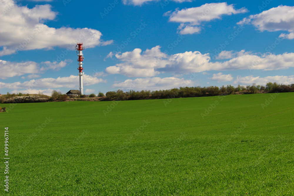 Green spring field with communication mast in background.