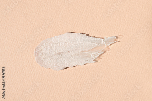 A smear of gray cosmetic clay for mud masks on a beige background, top view. Product for body care and facial skin cleansing.