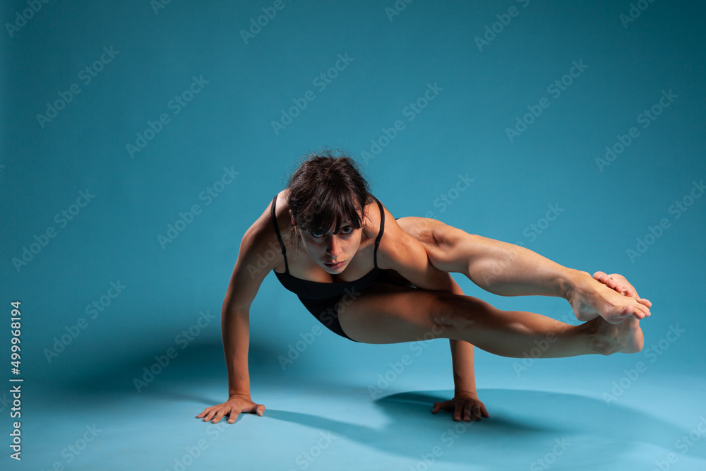 Active athletic woman standing in hands working at arm balance in studio with blue background. Personal trainer practicing gym exercices stretching body muscles during sport workout Active athletic woman standing in hands working at arm balance in studio with blue background. Personal trainer practicing gym exercices stretching body muscles during sport workout