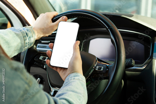 Woman sitting in car and holding smartphone with blank white screen