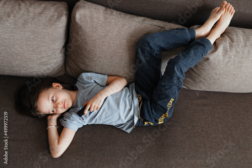The child is bored at home lying on the couch and watching TV all day
