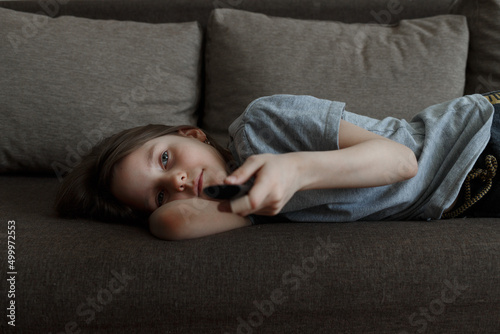 The child is bored at home lying on the couch and watching TV all day