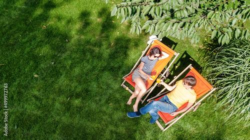 Foto Young couple relax in summer garden in sunbed deckchairs on grass, woman and men