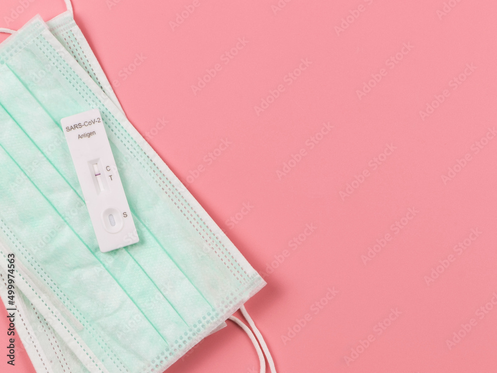 flat lay of Covid-19 negative test result antigen test kit (ATK) on medical face masks  on pink background with copy space.