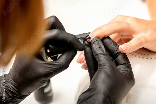 Manicure painting process. Manicure master paint the nails with transparent varnish in a nail salon  close up