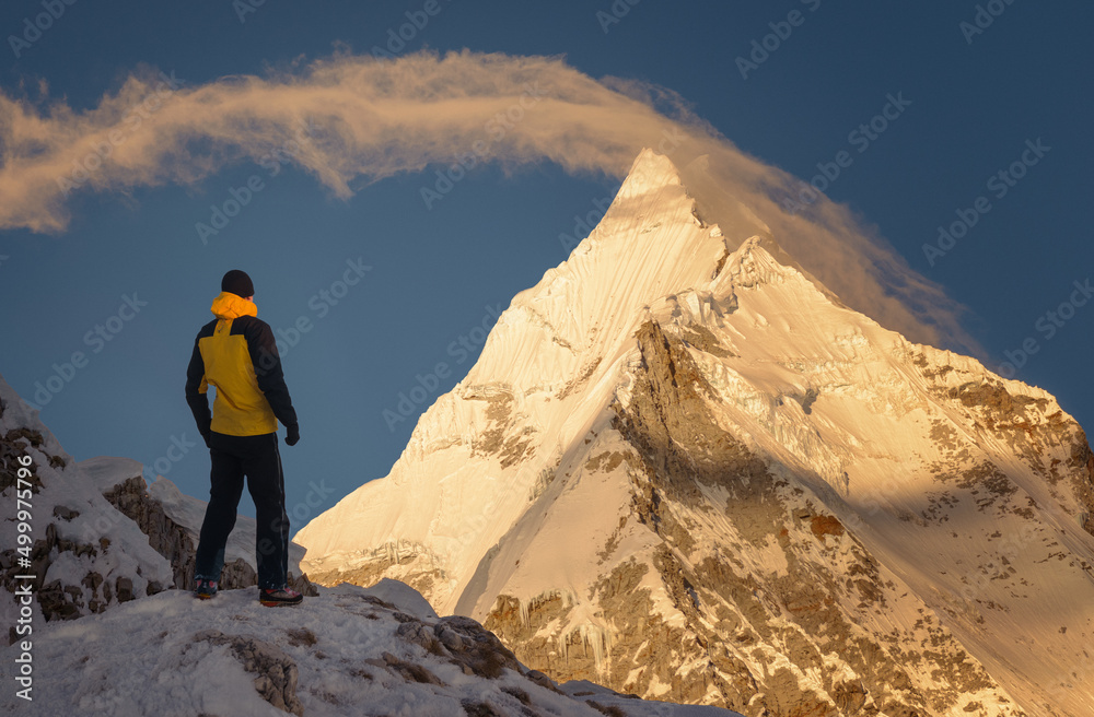 Man standing up with confidence in front of a majestic mountain peak in the morning at sunrise 