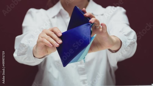 Faceless close-up of a woman holding a purple purse into the camera, opening her pocket and turning it over to show the lack of money