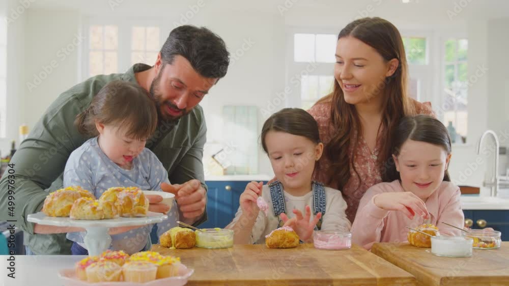 Family with Down Syndrome daughter sitting around table in kitchen at home decorating cakes together - shot in slow motion Family with Down Syndrome daughter sitting around table in kitchen at home decorating cakes together - shot in slow motion