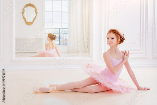 Little ballerina girl in a pink tutu and pointe shoes posing in white studio