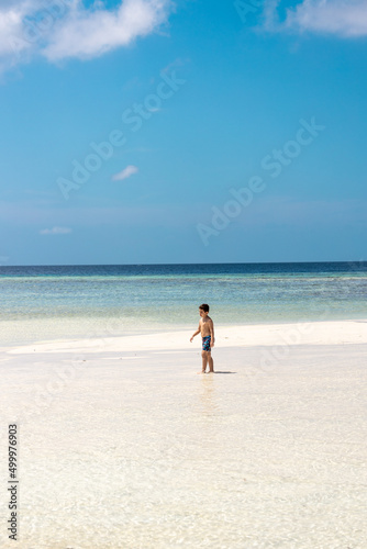 Little boy walking alone on a beach of turquoise water