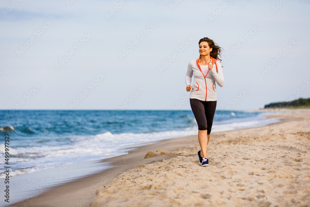 Young woman running, jumping on beach
