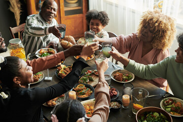 African big family toasting with glasses with lemonade while having holiday dinner together at table at home