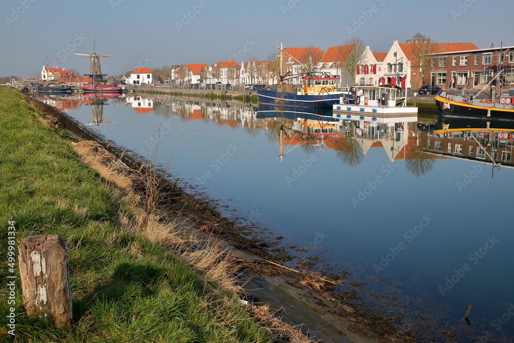Reflections of boats and historic buildings along Nieuwe Haven (New Harbor) close to Zuidhavenpoort  in Zierikzee, Zeeland, Netherlands, with a windmill in the background