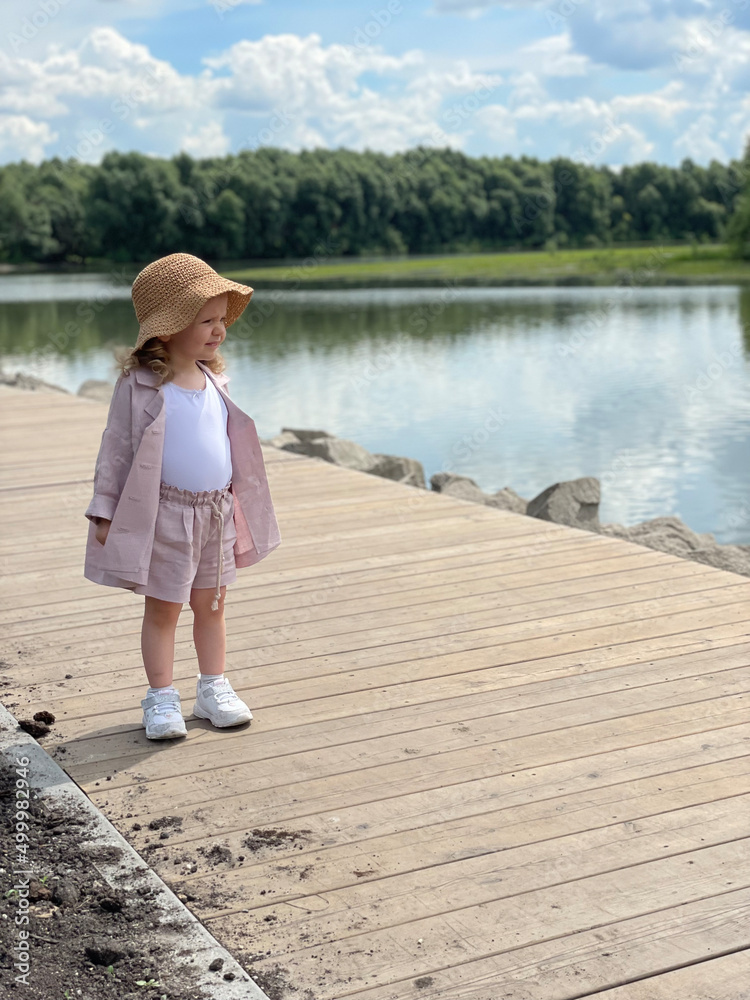 Baby girl in pin clothes and a straw hat in Park near the River