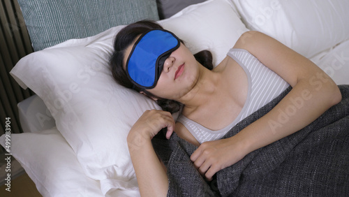 young female lying on white bedding with a sleeping mask, nearly waking up at dawn. authentic lifestyle. health and wellness concept.