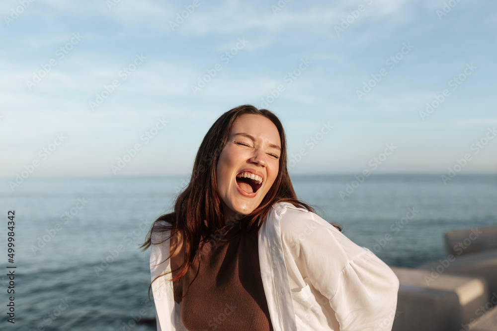 Outdoorsy brunette laughing with her eyes closed by the seaside Outdoorsy brunette laughing with her eyes closed by the seaside