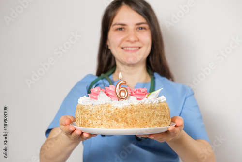 The doctor or nurse holds a birthday cake with the number six for the anniversary of the opening of the clinic
