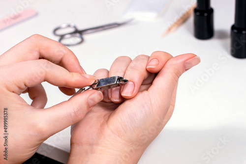 Young Caucasian woman making self manicure at home with the help of tools for nail procedures.