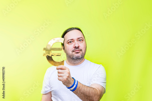 An adult, unshaven man holds a golden euro sign in his hand. A simple middle-aged worker with a national currency sign. Bracelet in the colors of the Israel flag.