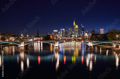 Frankfurt skyline and illuminated Ignatz Bubis bridge reflecting in the Main river at night.