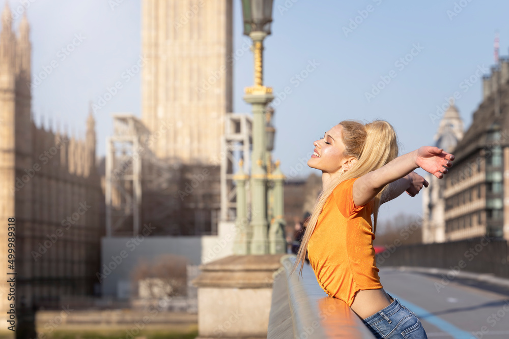 A happy tourist woman stands on the Westminster Bridge in London and enjoys the view over the City during her sightseeing trip