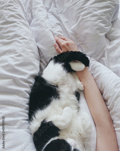 A woman sleeps in a white bed and hugs a cat