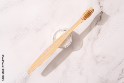 Bamboo toothbrush and mineral toothpowder on white marble table background. Natural bath products, organic dentifrice. Mockup image, flat lay