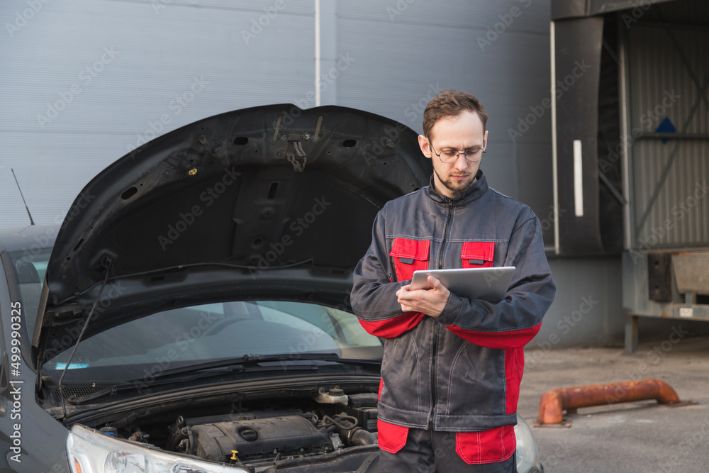 Caucasian mechanic in uniform using tablet pc at car repair station. Car maintenance Caucasian mechanic in uniform using tablet pc at car repair station. Car maintenance