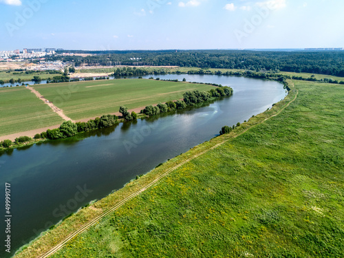 Large green field and trees near tranquil river in spring photo