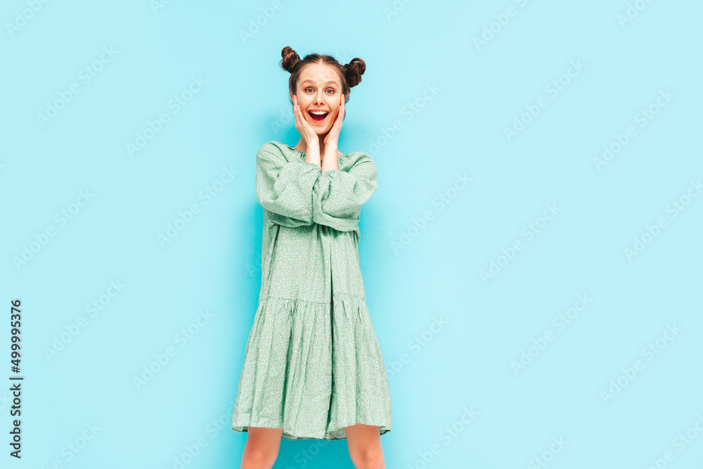 Young beautiful smiling female in trendy summer green dress. Sexy carefree woman with two horns hairstyle posing near blue wall in studio. Positive model having fun. Shocked and surprised Young beautiful smiling female in trendy summer green dress. Sexy carefree woman with two horns hairstyle posing near blue wall in studio. Positive model having fun. Shocked and surprised