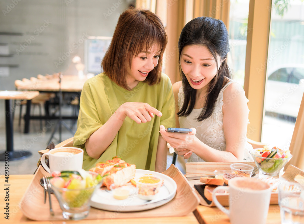 Young women sitting in restaurant looking at mobile phone and smiling Young women sitting in restaurant looking at mobile phone and smiling