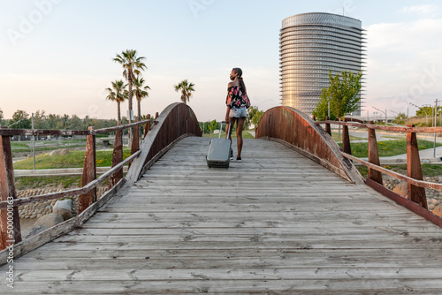 woman with face mask cross a wooden bridge with suitcase © Ana Sofía