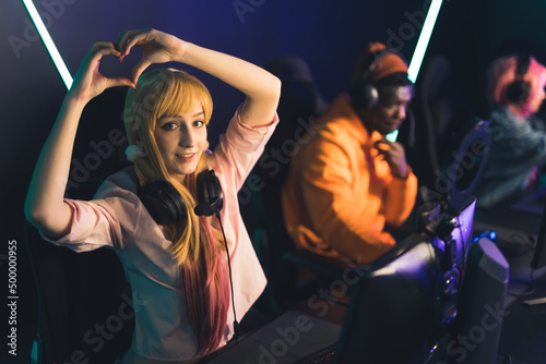 Young caucasian adorable female gamer influencer showing heart gesture with two hands and looking at camera. Internet cafe concept. High quality photo