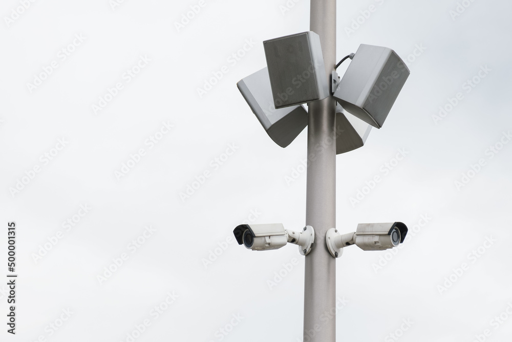 Two small white CCTV cameras and loudspeaker speakers on a pole . Security, video surveillance, face recognition. Providing security in a public place. Two small white CCTV cameras and loudspeaker speakers on a pole . Security, video surveillance, face recognition. Providing security in a public place.