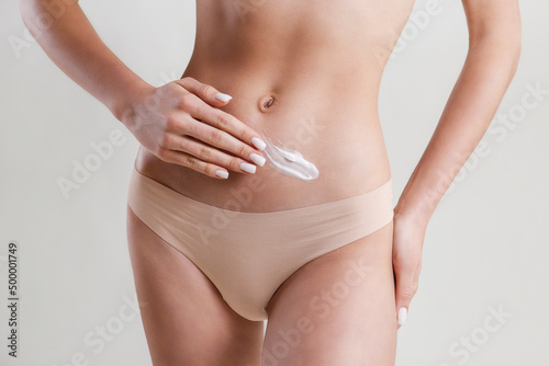 Studio shot of fit woman over isolated white background wearing only lingerie, applying moisturizing cream. Female in white underwear using a skincare product. Copy space for text, close up. © Evrymmnt