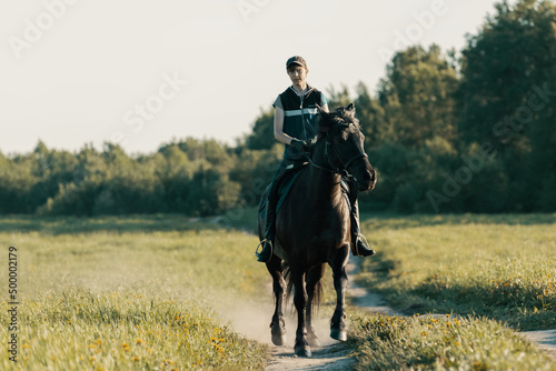 Teenage girl trotting on horse on country road.