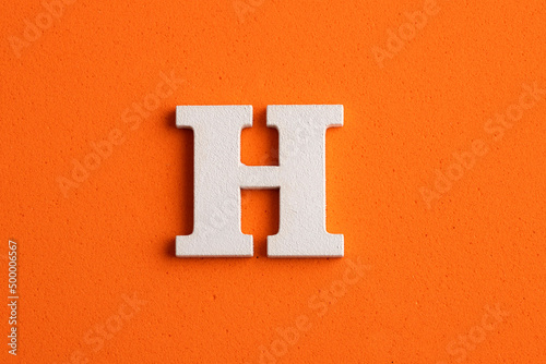 White wooden capital letter H on orange foamy background photo