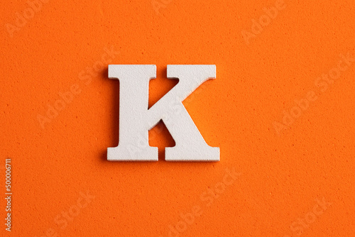 Alphabet letter K - White wood piece on orange foamy background