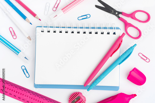 Notebook with white blank with colorful stationery on white desktop. Education concept. Mockup, directly above.
