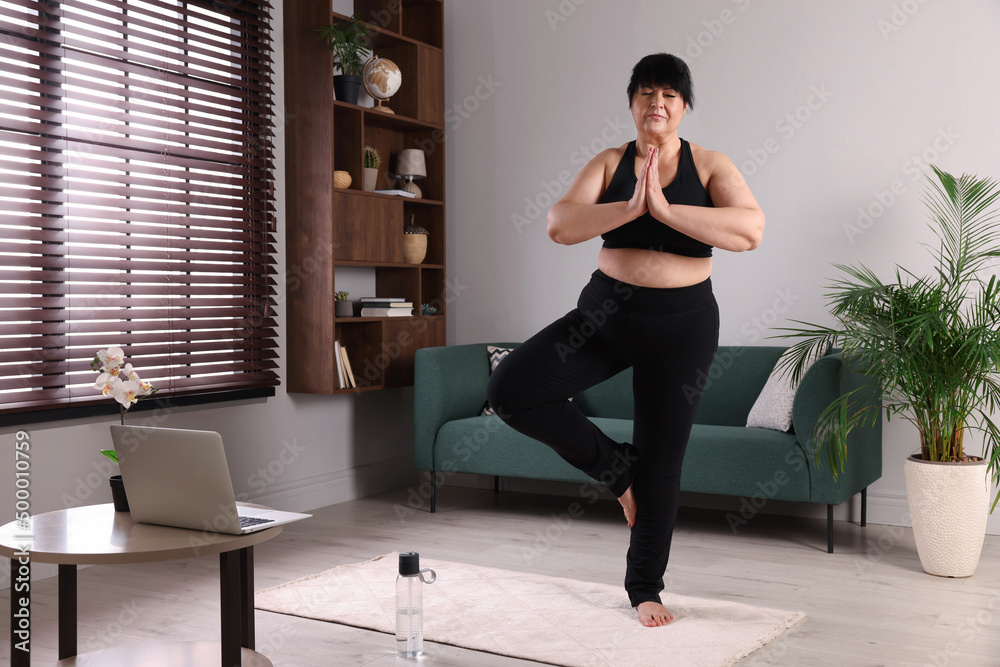 Obraz premium Overweight mature woman practicing yoga on rug at home