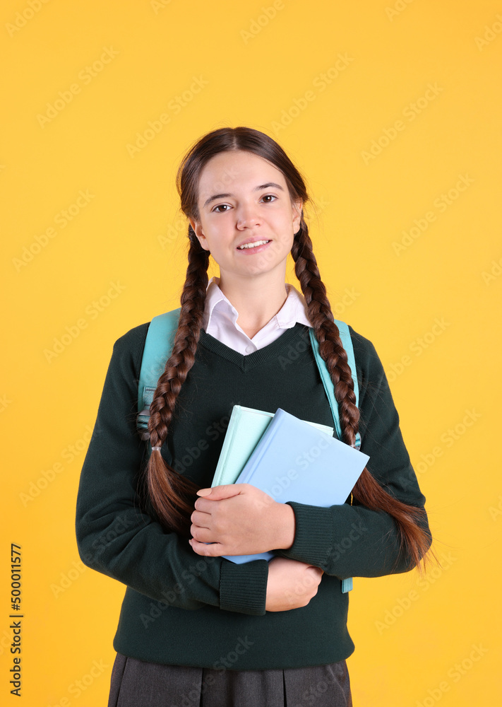 Obraz premium Teenage girl in school uniform with books and backpack on yellow background