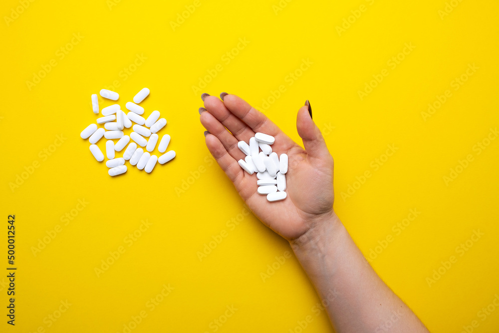 Woman's hand with white pills on a yellow background top view.