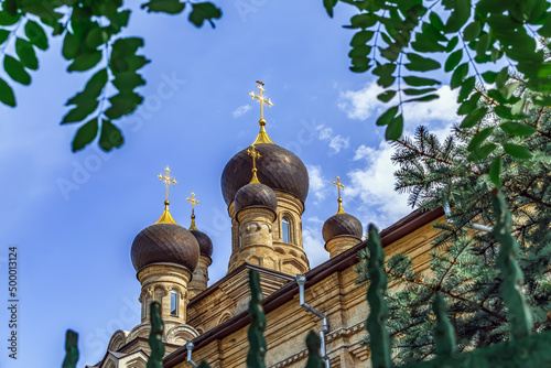 Towers with domes and golden crosses of Cathedral of Our Lady Mother of Kasperovskaya on the blue sky among the greenery in Mykolaiv, Ukraine. Part of Ukrainian Orthodox Church architecture close-up photo